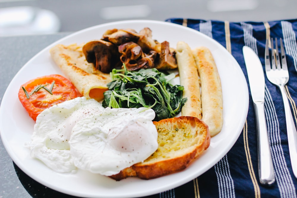 스테인레스 스틸 버터 나이프와 포크 옆에있는 흰색 세라믹 접시에 햇볕이 잘 드는 사이드 업 계란
