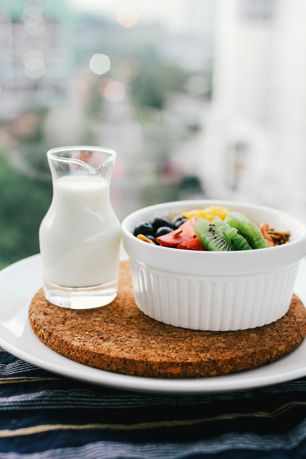 ensalada de frutas dentro de un tazón junto al vaso de leche en una tabla marrón