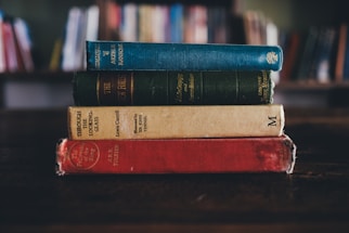 A stack of colorful novels on a wooden table.