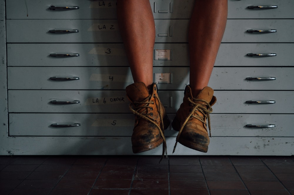 person wearing brown work boots on cabinet