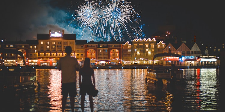 two people standing beside body of water watching fireworks