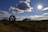 A woman inspecting farm equipment in a rural yard on a bright day.
