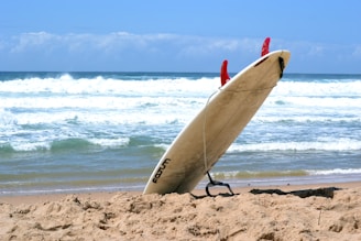 Close-up of a surfboard resting on the sandy beach with ocean waves in the background.