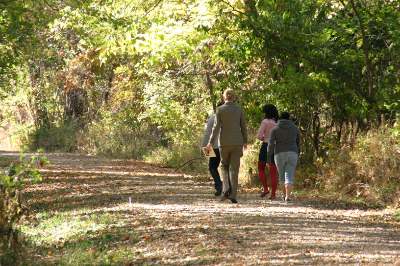 A group of women smiling and walking together on a sunlit forest trail.