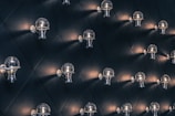 Numerous wall-mounted light fixtures arranged in a geometric pattern against a dark, diamond-patterned wall. Each fixture emits a soft, warm glow, illuminating the space subtly.