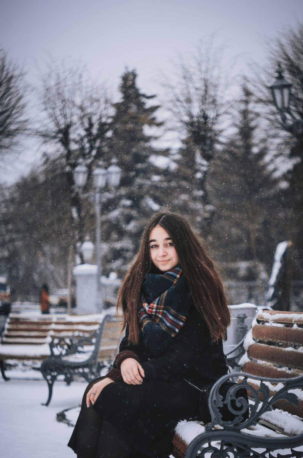 mulher sentada no banco de madeira marrom durante o dia nevado