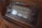 A vintage radio with a classic design featuring a large tuning dial and various frequency numbers. The radio has a wooden casing and multiple control knobs. It displays a variety of international radio stations, indicative of its age and style.