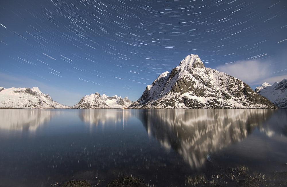 Zeitrafferfotografie von Bergalpen in der Nähe von Wasser mit Sternen