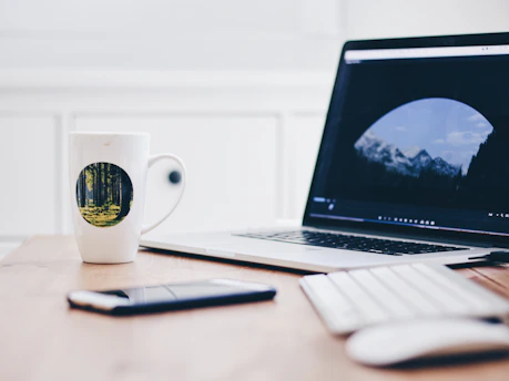 A sleek, modern workspace with a laptop, notepad, and a steaming cup of coffee, set against a backdrop of mountain peaks at dawn.