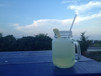 Close-up of a mason jar filled with fresh kefir next to healthy green leaves, on a wooden table with natural light.