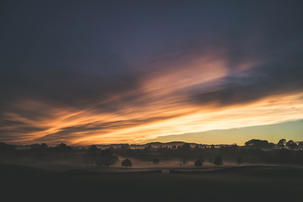 silhouette of trees and mountain under cloudy sky