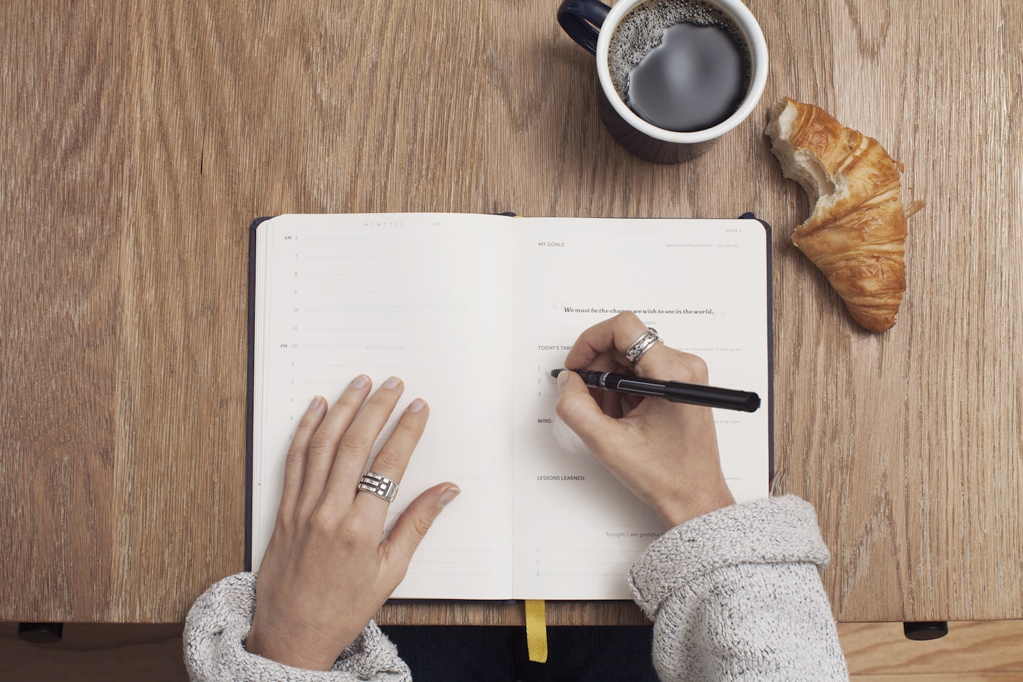 mani di donna che scrive su un'agenda con caffè e croissant sul tavolo di legno