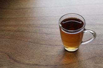 Steaming cup of amber tea resting on a weathered table with soft sunlight.