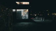 Night shot of a small business storefront illuminated with security cameras visible.