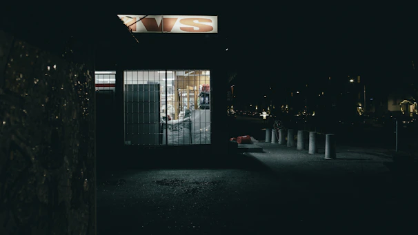 A well-lit storefront being treated carefully by a pest control expert late in the evening.