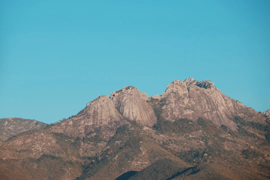 Researchers collecting rock samples in a rugged mountain landscape under a clear blue sky.