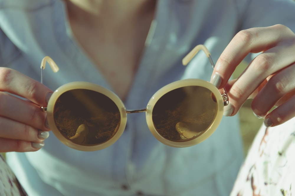 mujer sosteniendo gafas de sol redondas durante el día