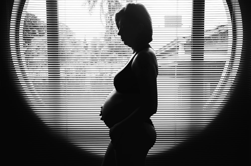 Fotografia da silhueta da mulher gravida perto da janela