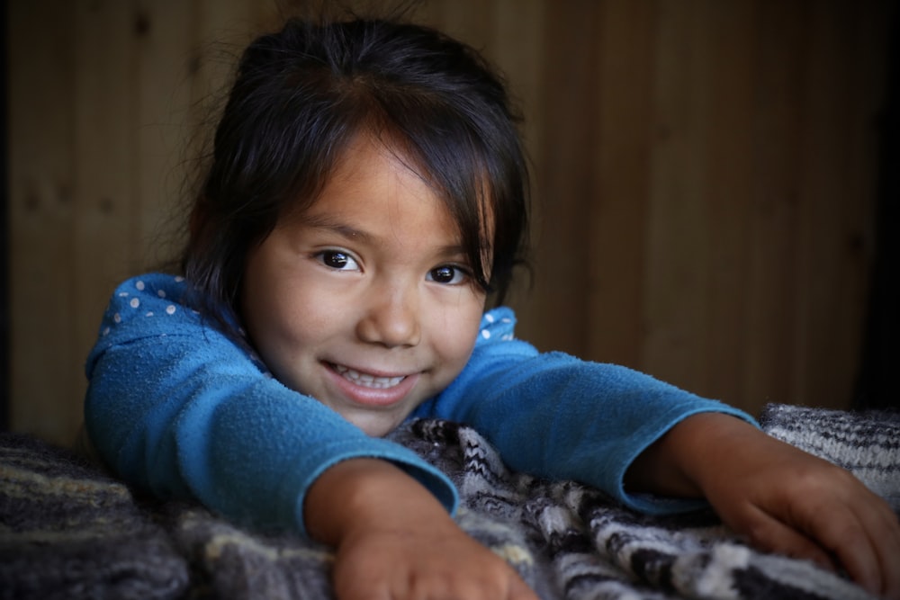 girl wearing blue sweater with hands on gray bedspread