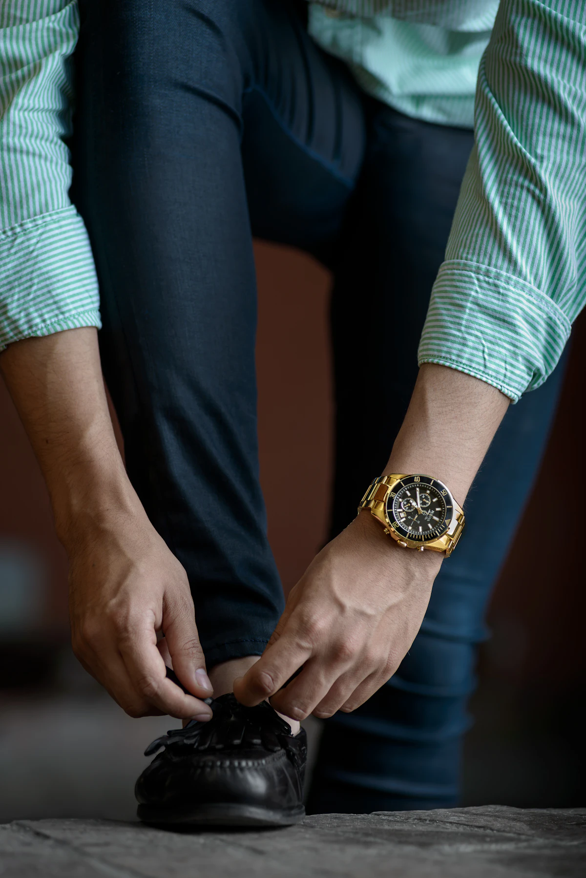 Man in a tailored shirt adjusting his cuff while wearing a gold watch