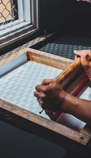 man holding printing screen near white window