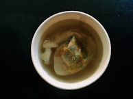 Close-up of herbal tea being poured into a glass cup with steam rising.