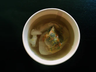 Close-up of steaming organic tea in a rustic cup surrounded by fresh herbs and tea leaves.