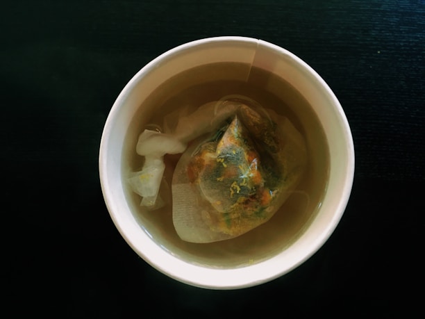Close-up of a steaming cup of richly brewed tea with tea leaves scattered nearby.