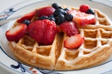 A steaming Belgian waffle topped with fresh strawberries and powdered sugar on a delicate plate.