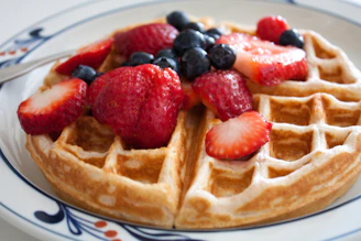A golden waffle topped with fresh berries and a drizzle of syrup on a white plate.