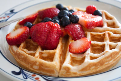A golden waffle topped with fresh berries and a drizzle of syrup on a white plate.
