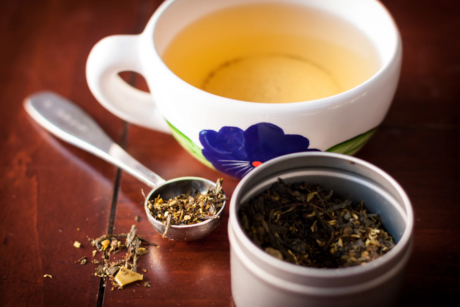 A cup of tea beside loose tea leaves on a wooden table