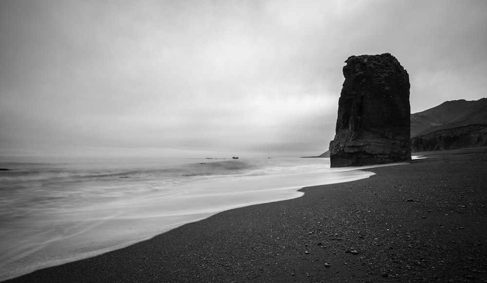 large rock on shore grayscale photography