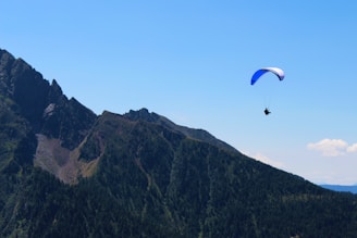 An inspiring image of a paraglider soaring high above green mountains under a clear blue sky.