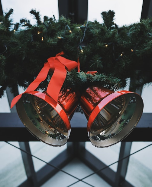 two red steel bells beside green Christmas decoration