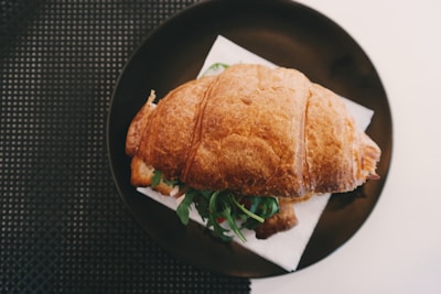 A warm croissant sandwich filled with melted cheese and fresh greens on a ceramic plate.