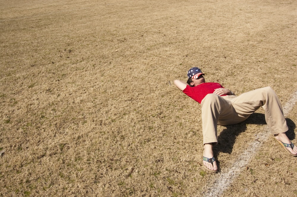 man in red top lying on lawn field during daytime