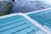 Two swimming pools with clear blue water are situated along a rocky coastline. The pools are enclosed with safety railings, and the ocean waves gently touch the shore nearby.