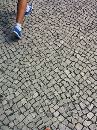 A close-up of feet walking on a sidewalk, avoiding obstacles.