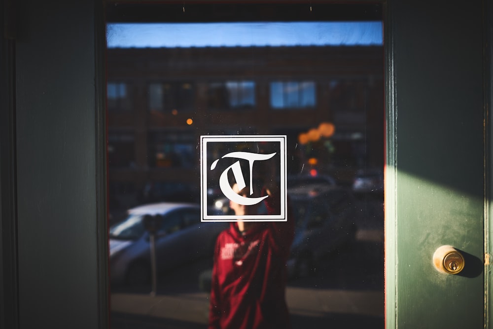 Person in red shirt in reflection of door window with lock and logo