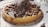 A delicious waffle topped with whipped cream, chocolate sauce, and chocolate shavings, served on a white plate with scattered chocolate droplets around it.