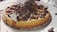 A delicious waffle topped with whipped cream, chocolate sauce, and chocolate shavings, served on a white plate with scattered chocolate droplets around it.