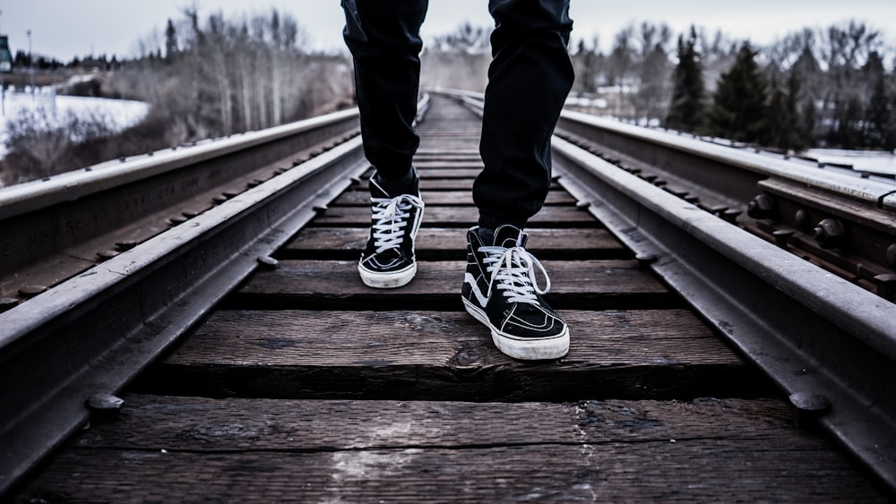 person wearing pair of black-and-white Vans Old Skool shoes walking on  brown train tracks during winter photo – Free Image on Unsplash