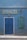 A blue facade with a large blue door and two green signs featuring white, bold text reading 'ANTIQUITES'. The signs seem to advertise buying, selling, and exchanging antiques, with additional contact information visible. A single wall-mounted light fixture is centered above the door.