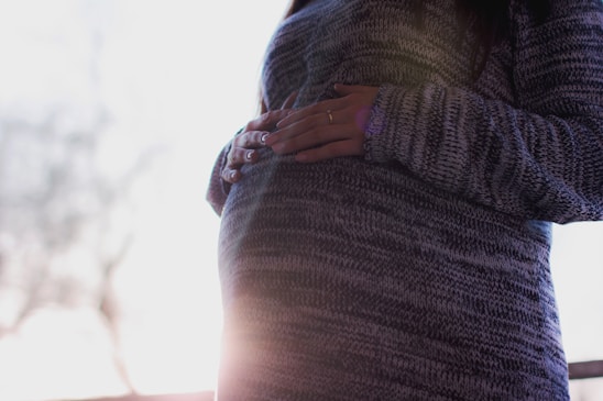 A serene pregnant woman gently cradling her belly, bathed in soft pink light with a champagne and gold gradient background.