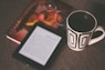 black E-book reader beside white and black mug
