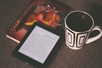 black E-book reader beside white and black mug