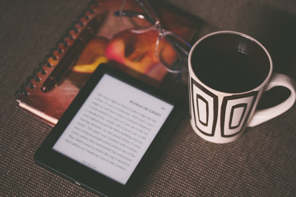 black E-book reader beside white and black mug