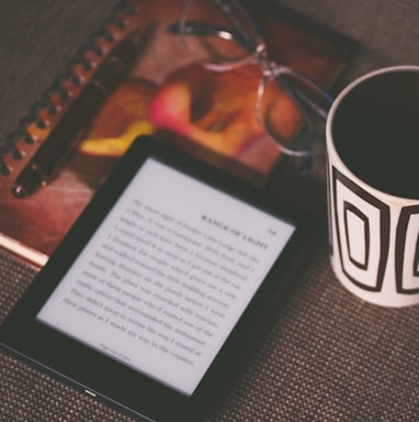 black E-book reader beside white and black mug