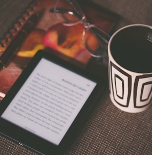 black E-book reader beside white and black mug